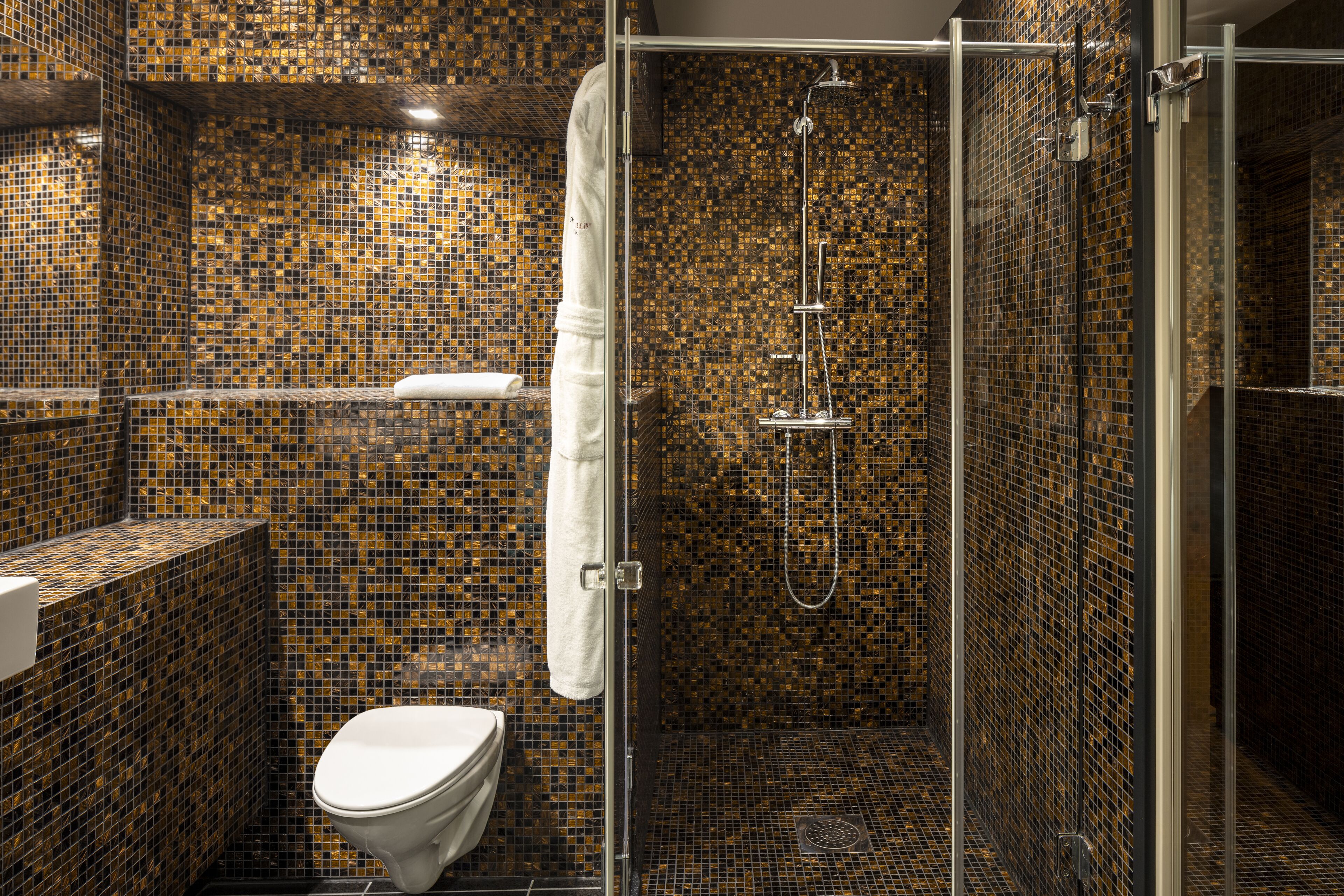 A bathroom with mosaic tile walls, a glass-enclosed shower, and a white toilet.