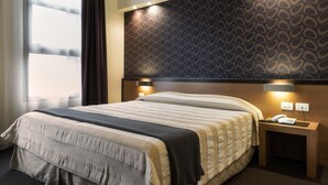 A hotel room with a large bed, a bedside table with a phone, and a patterned wall. - Hc3 Hotel (Bologna)