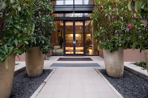 A hotel entrance with a tiled pathway leading to a glass door, surrounded by large potted plants. - Hc3 Hotel (Bologna)