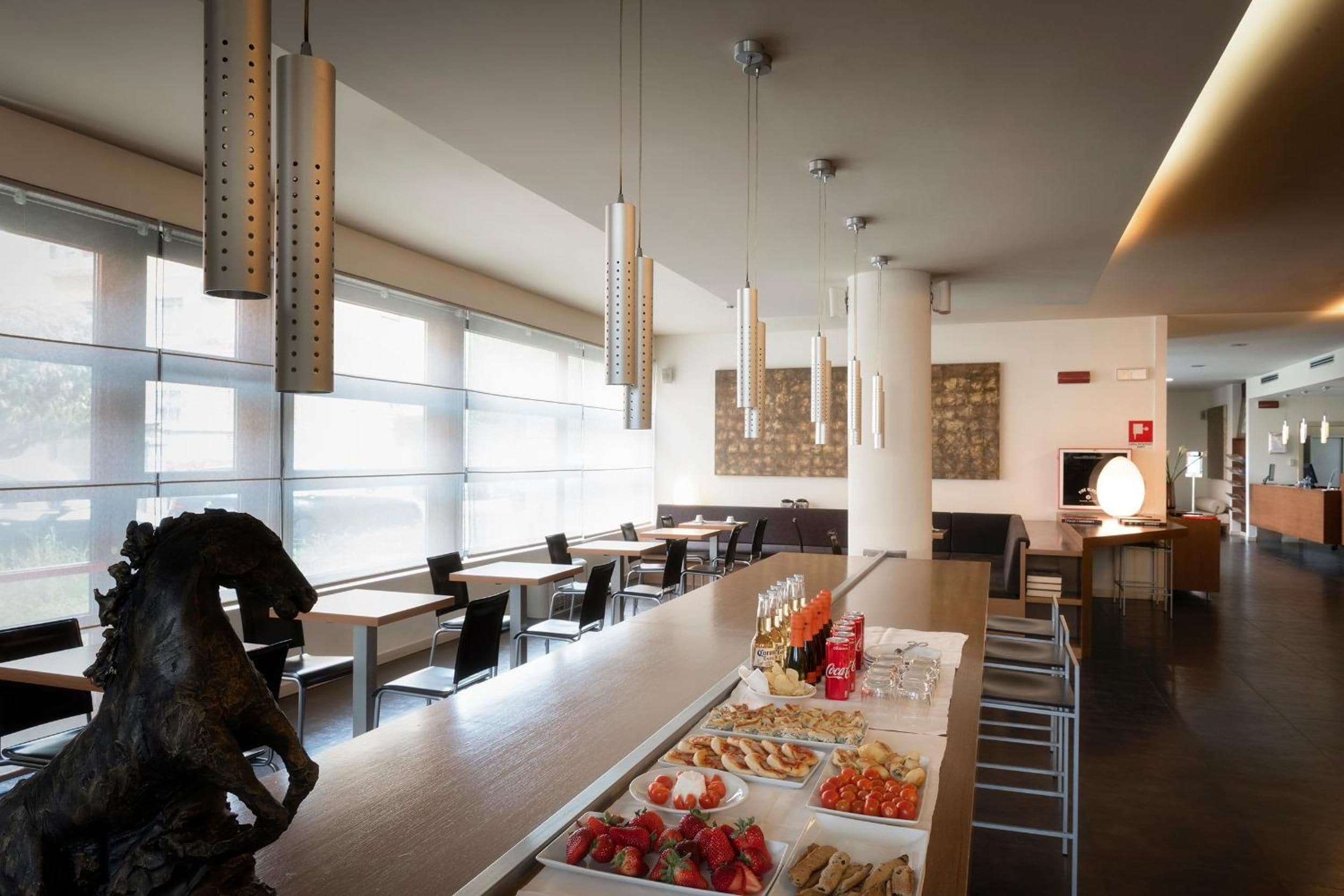 A modern dining area with a long counter, various food items, and hanging pendant lights.