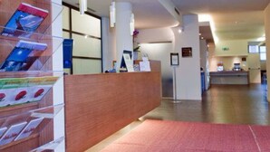 A reception area with a wooden reception desk, brochures, and a red carpet. - Hc3 Hotel (Bologna)