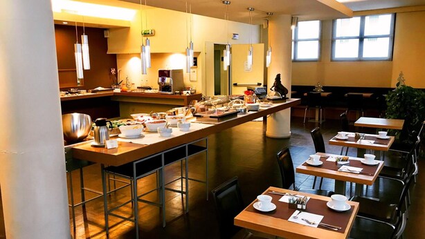 A modern dining area with a buffet setup, multiple tables, and a central serving station. - Hc3 Hotel (Bologna)
