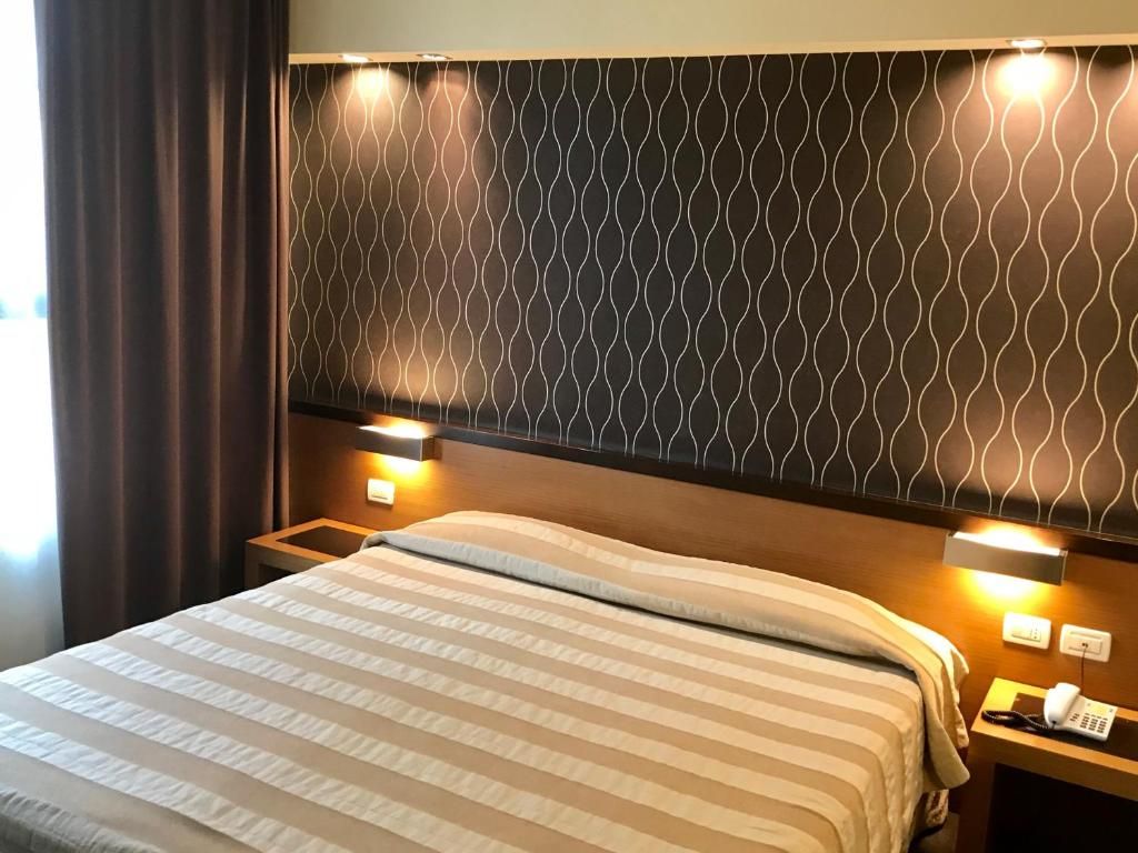 A hotel room with a bed, two bedside lamps, a telephone, and a patterned headboard.
