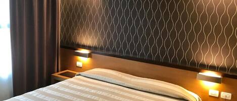 Habitación de hotel con una cama, dos lámparas de noche, un teléfono y un cabecero estampado.