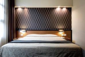 A hotel room with a bed, two bedside tables, a headboard with a patterned design, and wall-mounted lights. - Hc3 Hotel (Bologna)