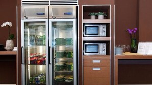 A minibar with a refrigerator and microwave, shelves with bottles, and a small potted plant. - Hc3 Hotel (Bologna)