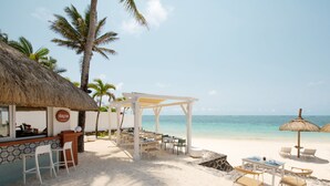 A beachside restaurant with a thatched roof, outdoor seating, and a view of the ocean. - Veranda Belle Mare - All Inclusive (Belle Mare)