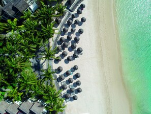 An aerial view of a beach with rows of umbrellas and palm trees.