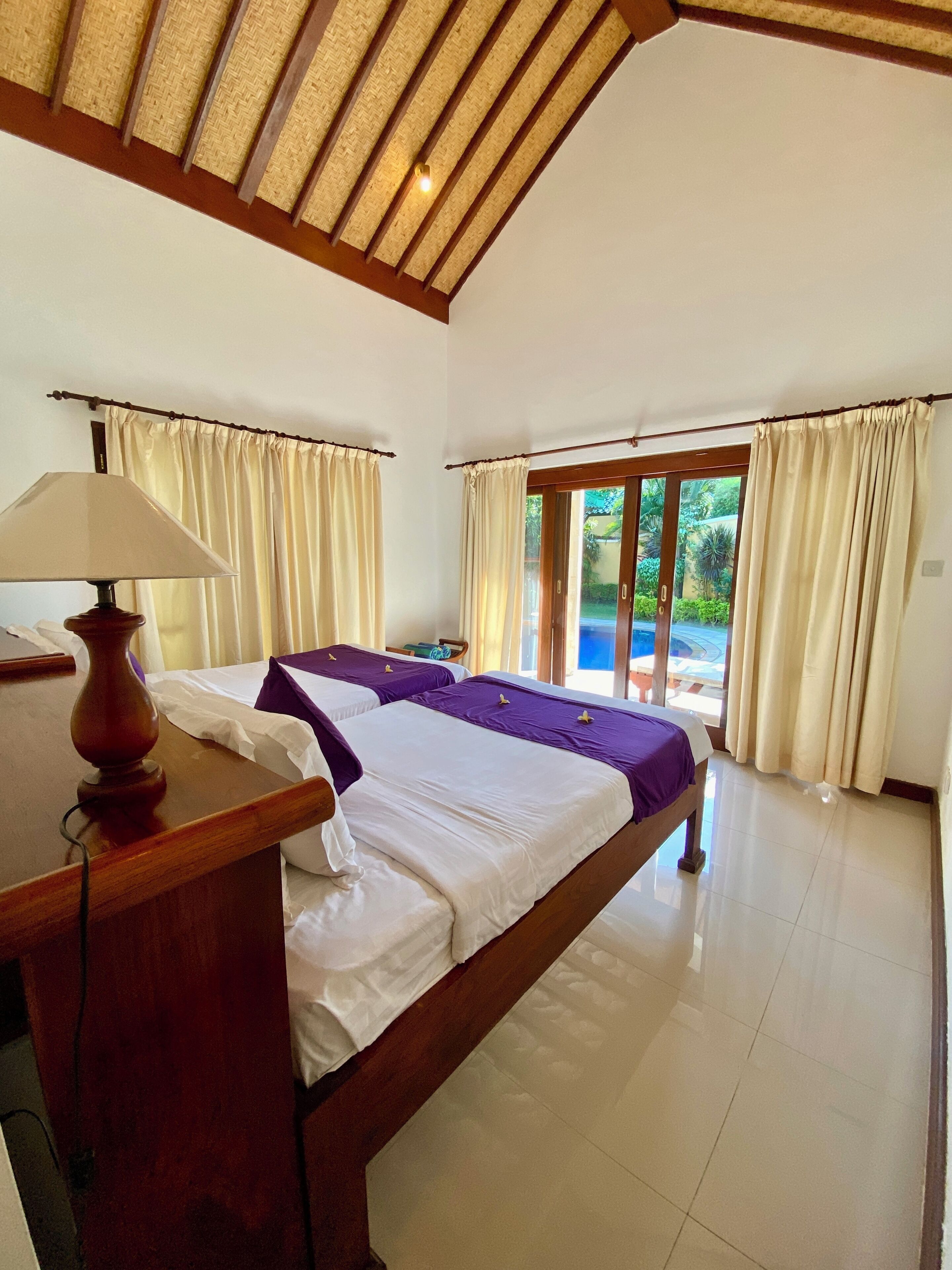 A bedroom with a bed, a desk with a lamp, and a view of the outdoors through a sliding door.