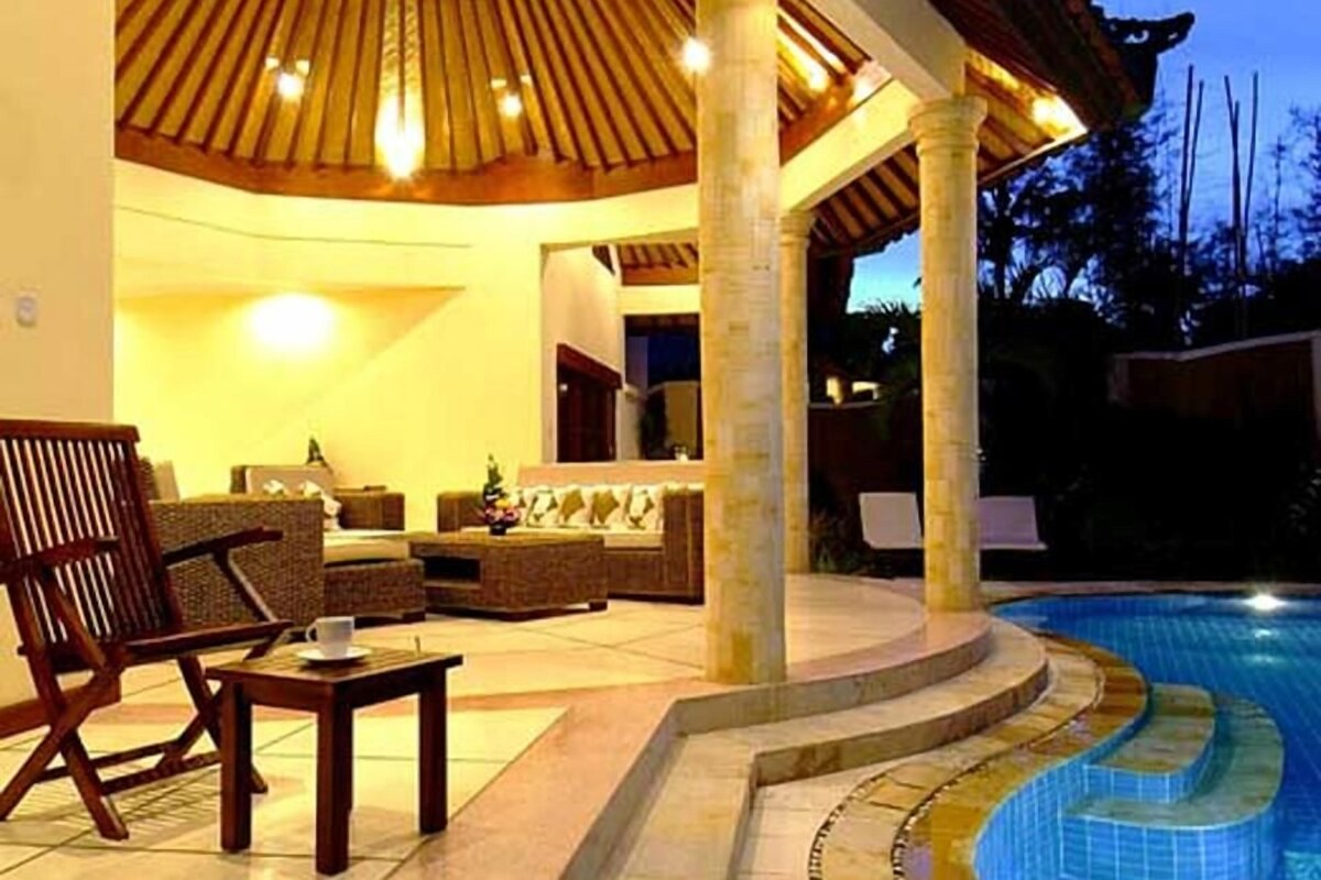 A poolside area with a covered seating area, a pool, and a view of the surrounding landscape.