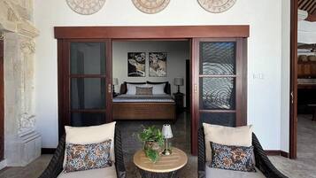 Una habitación con dos sillones de mimbre, una pequeña mesa redonda con una planta y una cama con vistas.