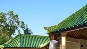 A chef grilling food outdoors near a pool with a traditional tiled roof and a dining area in the background. - Bali Emerald Villas (Denpasar)