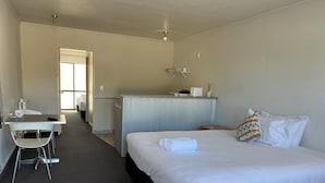 A hotel room with a bed, a desk, a chair, a small kitchenette, and a bathroom. - Karaka Tree Motel (Taupo)