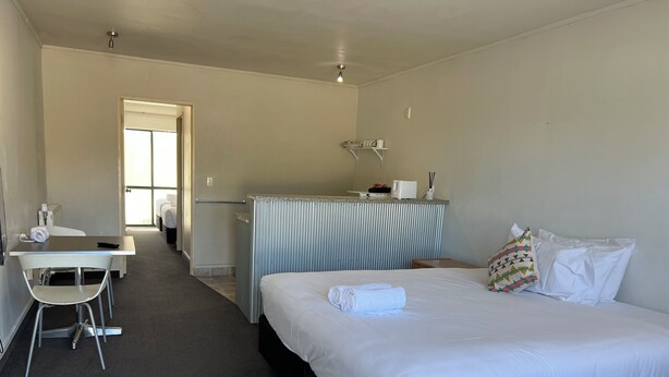 Una habitación de hotel con cama, escritorio, silla, kitchenette pequeña y baño.