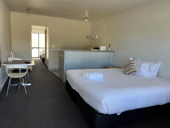 A hotel room with a bed, a desk, a chair, a small kitchenette, and a bathroom. - Karaka Tree Motel (Taupo)