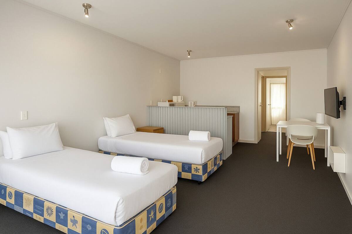A hotel room with two beds, a desk, a chair, a TV, and a bathroom door.