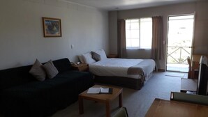 A hotel room with a bed, a sofa, a small table, and a chair. - Karaka Tree Motel (Taupo)