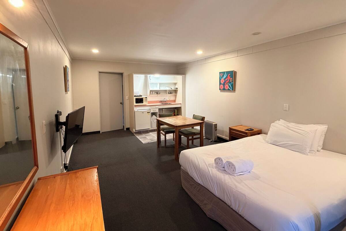 A hotel room with a bed, a desk, a chair, a small kitchenette, and a bathroom.