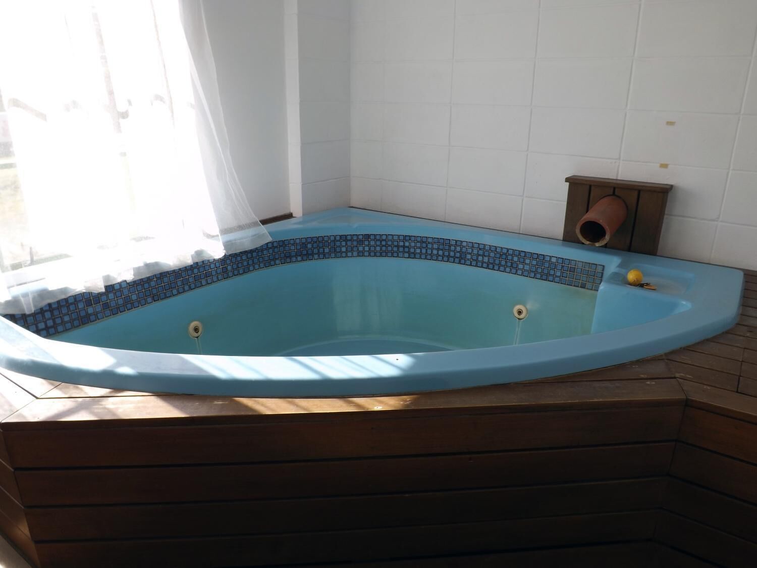 A corner hot tub with a blue mosaic border, wooden steps, and a small speaker.