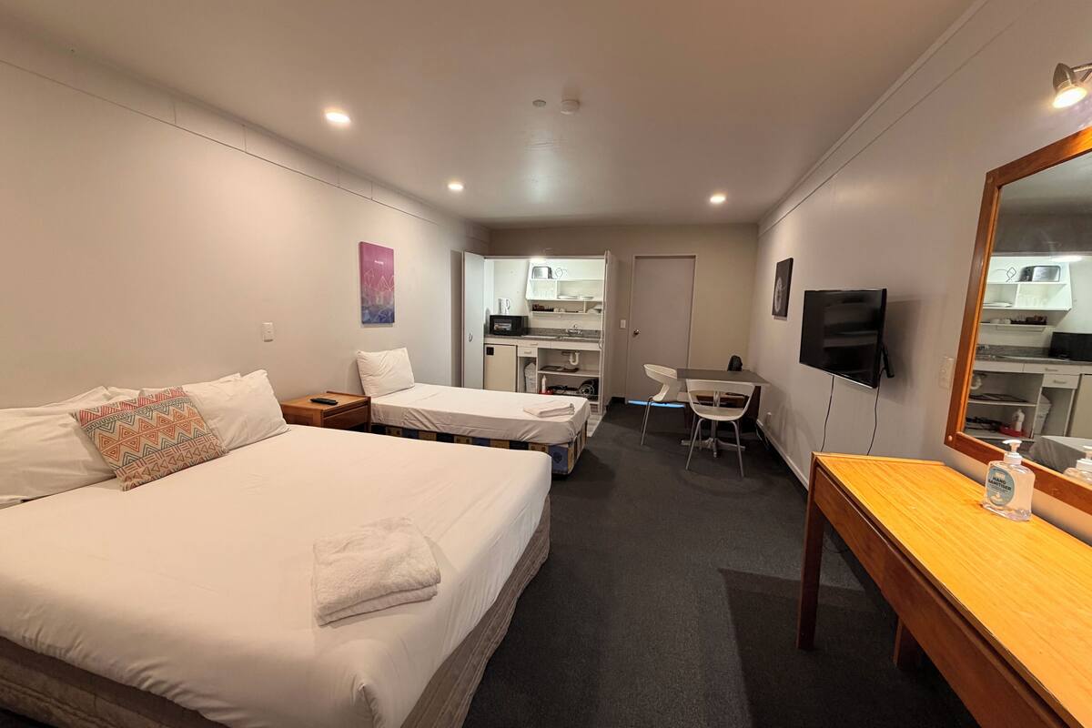 A hotel room with a bed, a desk, a chair, a TV, and a kitchenette.