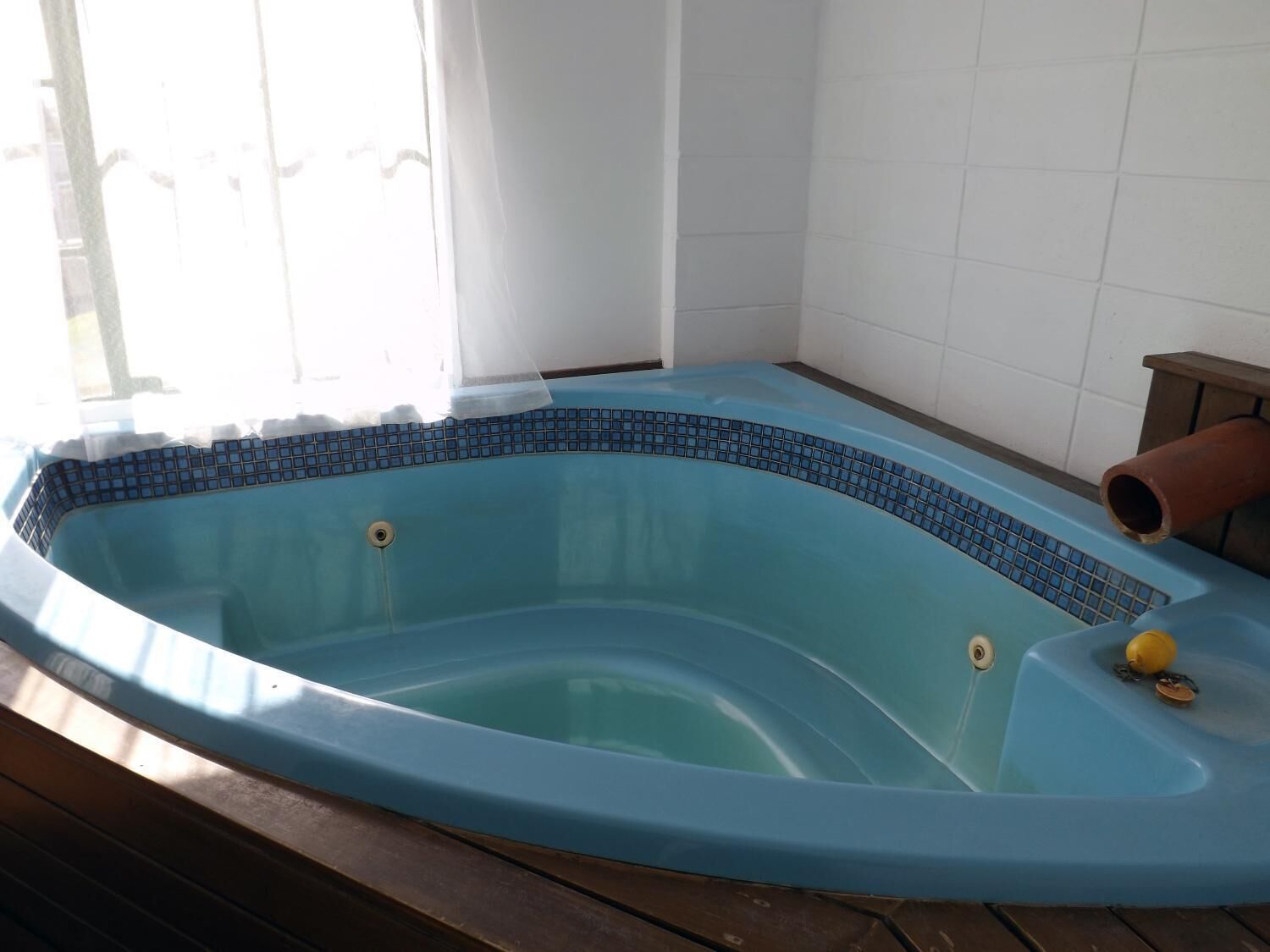 Un bain à remous bleu avec un bord carrelé, un drain et un petit objet jaune sur le côté.