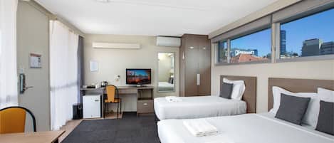 A hotel room with two beds, a desk, a chair, a television, and a window with a city view.