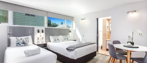Una habitación de hotel moderna con dos camas, un área de comedor y vistas al exterior.