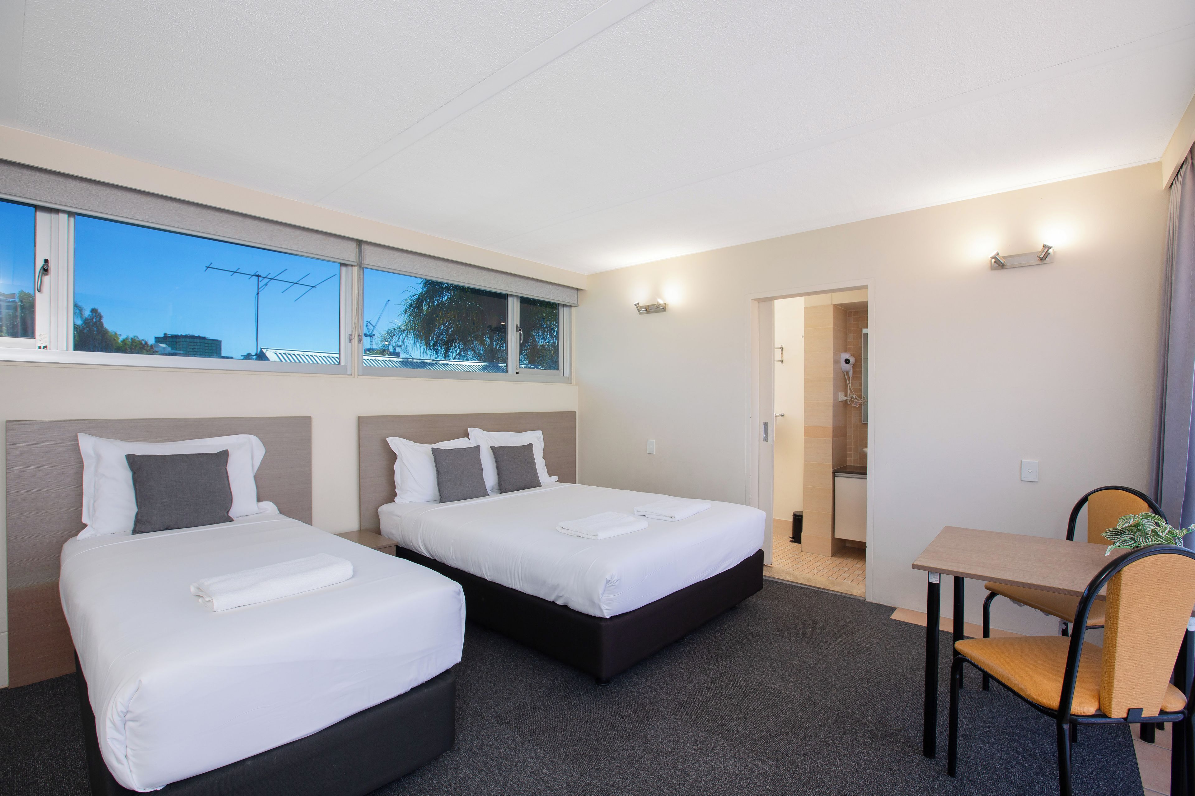 Quarto de hotel com duas camas, uma escrivaninha e zona de chuveiro.
