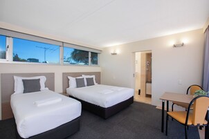 Habitación de hotel con dos camas, un escritorio y zona de ducha.