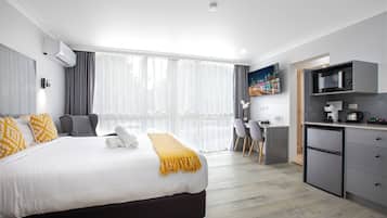 A modern hotel room with a large bed, a desk, a microwave, and a refrigerator.
