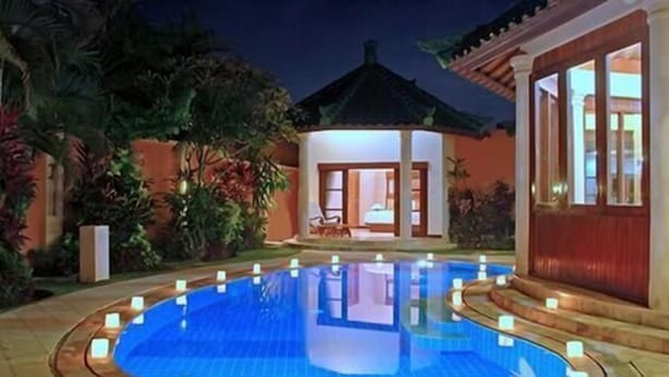 A swimming pool with a tiled deck, surrounded by tropical plants and a building with a tiled roof. - Bali Jade Villas (Denpasar)