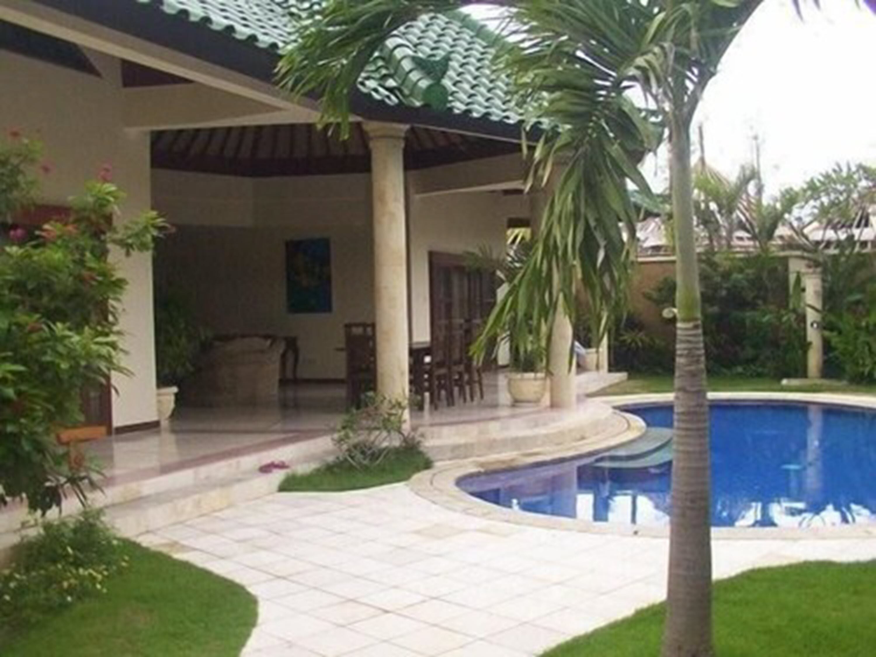 Uma área à beira da piscina com um deck revestido de azulejos, palmeiras e um gramado bem cuidado.