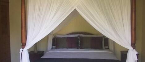 A four-poster canopy bed with white drapes, a wooden headboard, and a dark-colored bedspread.