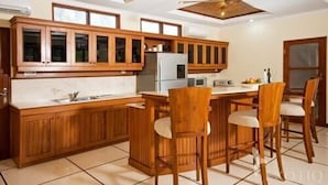 A kitchen with wooden cabinets, a central island with bar stools, and a ceiling fan. - Bali Jade Villas (Denpasar)