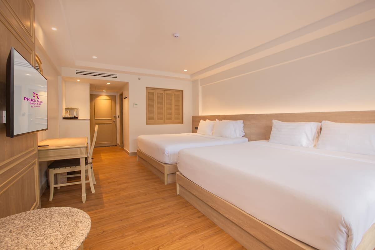 A hotel room with two single beds, a desk, a chair, and a television.