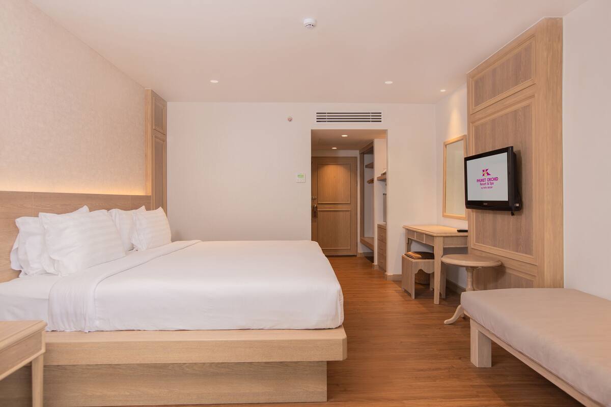 A hotel room with a large bed, a bedside table, a small desk, and a TV mounted on the wall.
