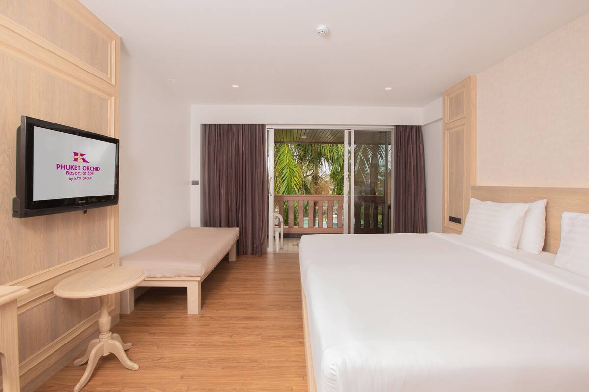 A hotel room with a large bed, a smaller bed, a TV mounted on the wall, and a balcony with curtains.