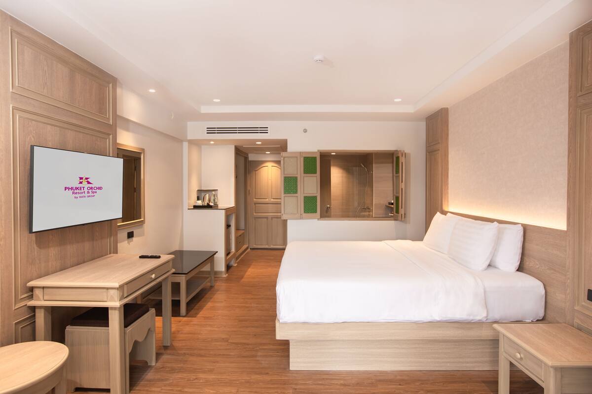 A modern hotel room with a bed, bedside tables, a desk, and a TV displaying the hotel name.