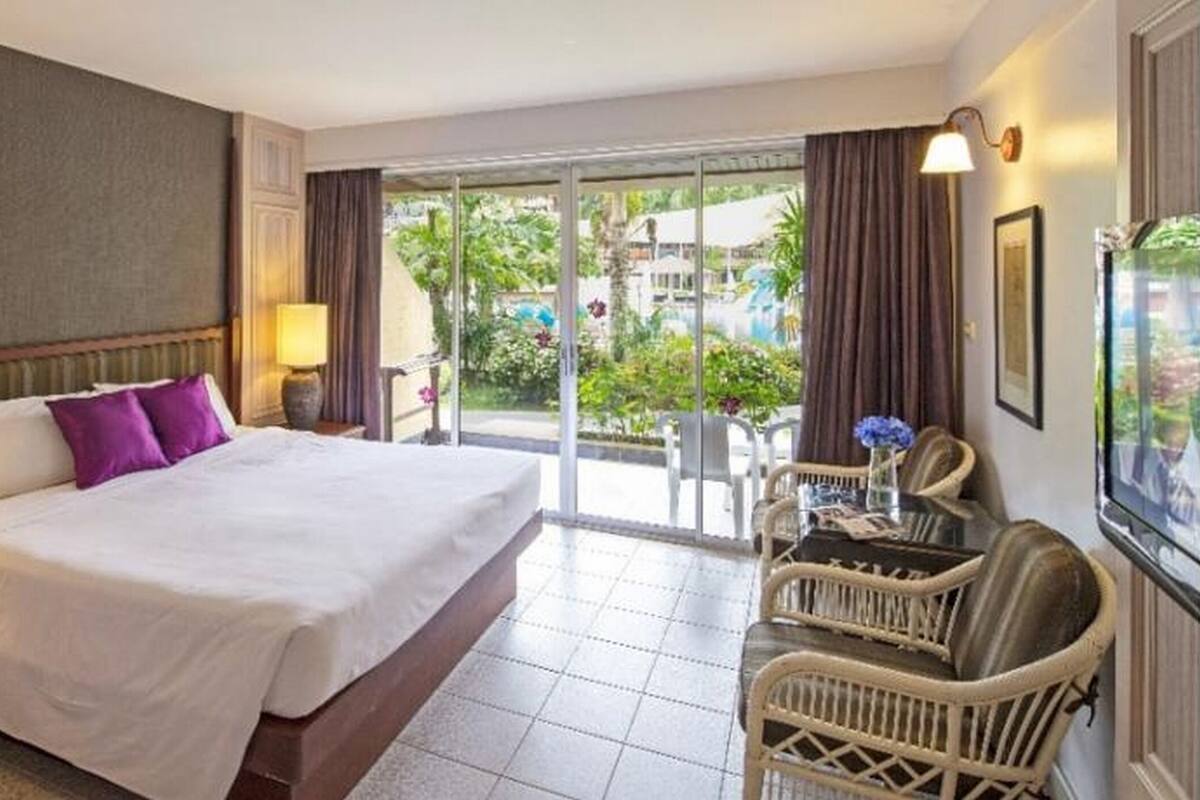 A hotel room with a large bed, a desk, a chair, and a view of the outdoors.