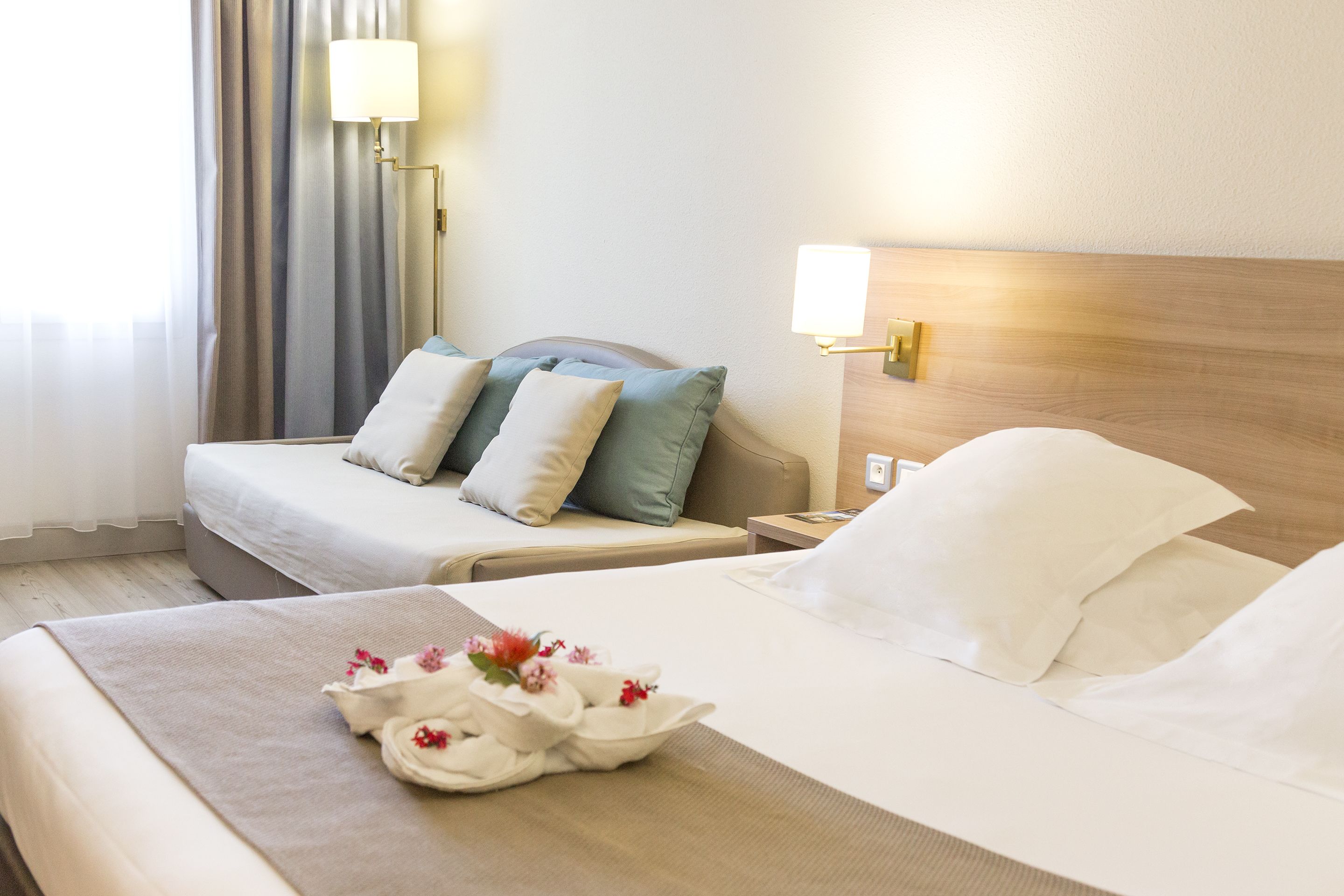A hotel room with a bed, a nightstand, a lamp, and a window with curtains.
