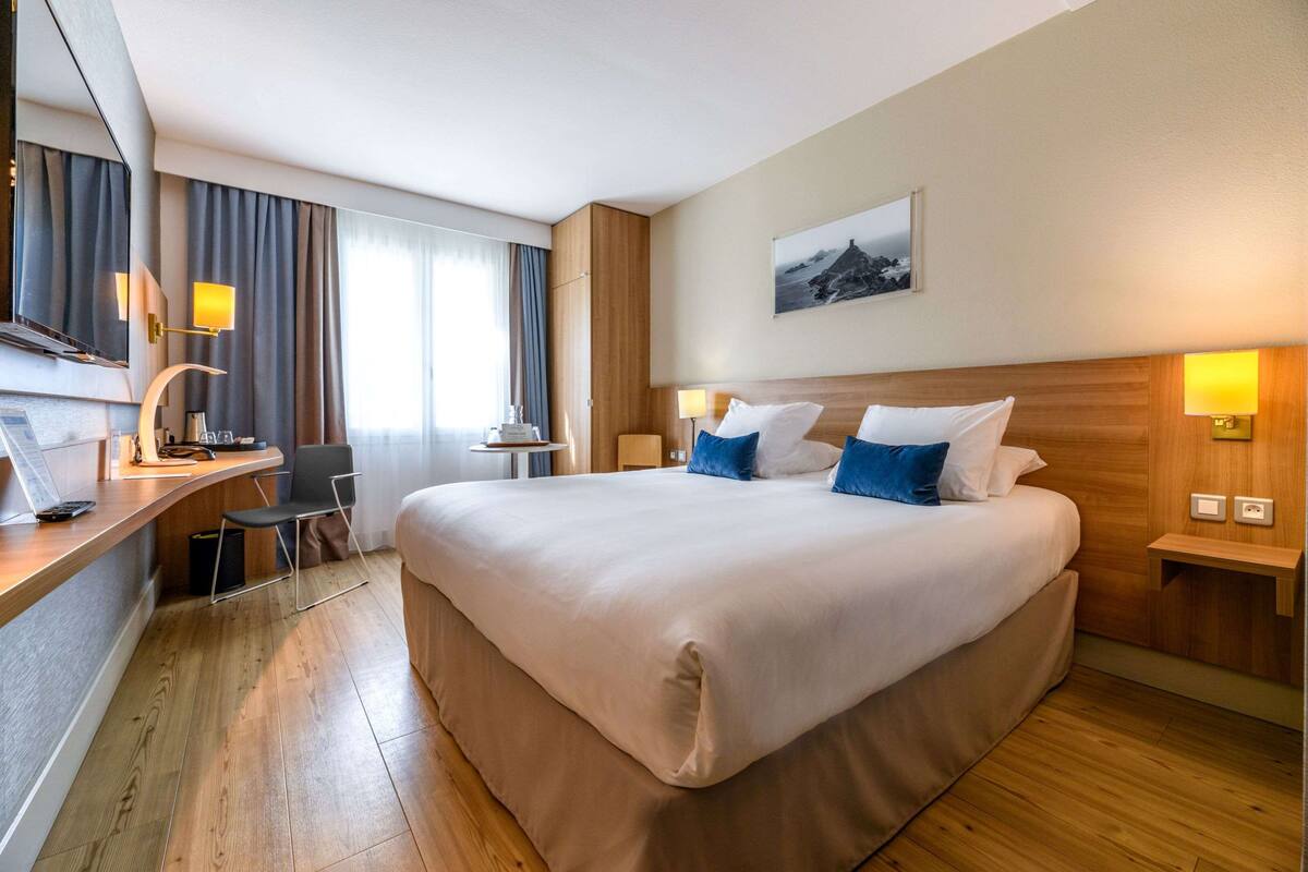 Ein Hotelzimmer mit einem großen Bett, einem Schreibtisch mit Stuhl, einem kleinen Tisch und einem Fernseher.