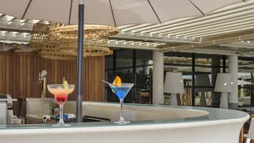 A bar area with two cocktails on a glass table, a wicker hanging light fixture, and a modern ceiling design.
