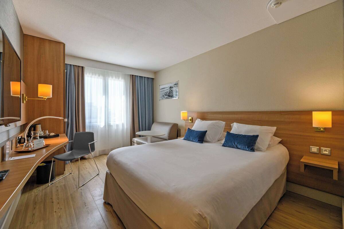 Ein Hotelzimmer mit einem großen Bett, einem Schreibtisch mit Stuhl, einem kleinen Tisch und zwei Nachttischlampen.