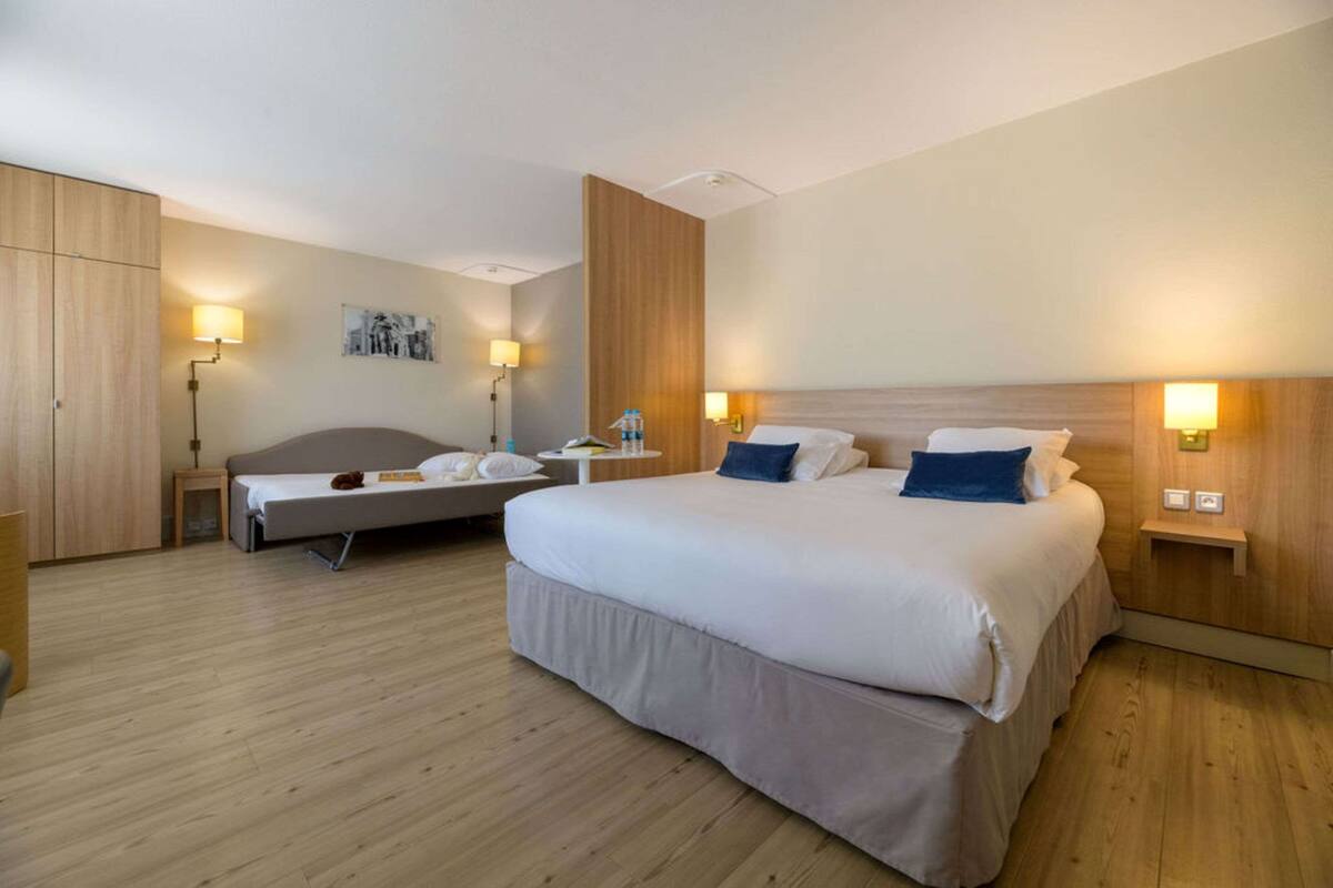 Ein Hotelzimmer mit einem großen Bett, einem kleineren Bett, Holzböden und zwei Nachttischen mit Lampen.