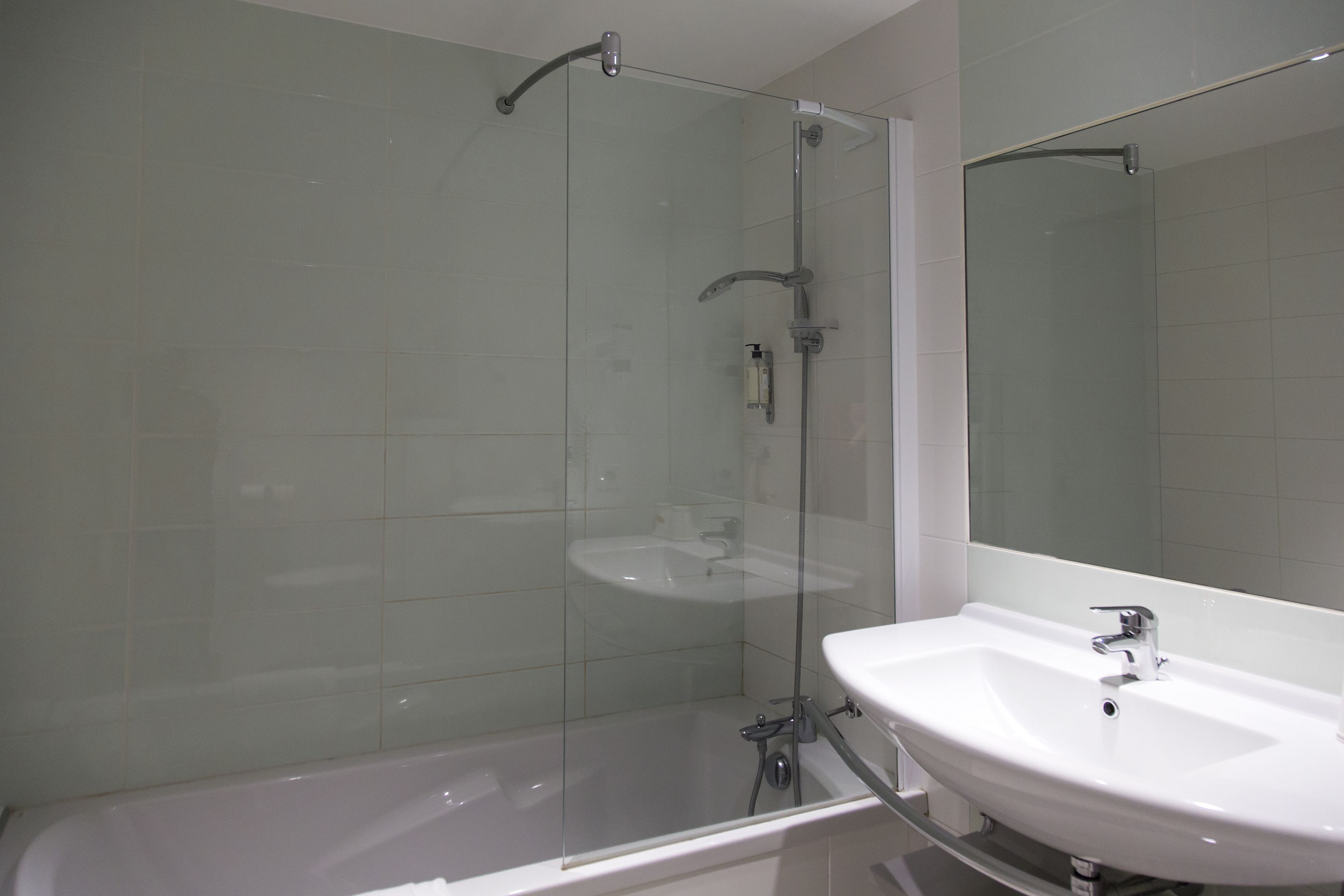 Un baño con ducha acristalada, un lavabo blanco y un espejo.