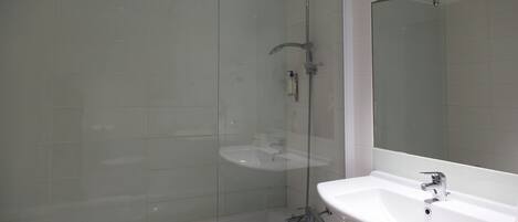 Un baño con ducha acristalada, un lavabo blanco y un espejo.