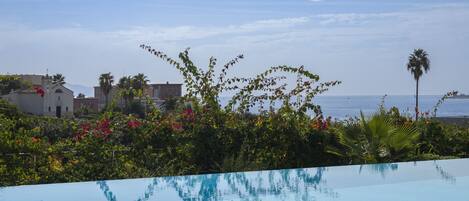 Una piscina azul y transparente con vista al mar y edificios al fondo.