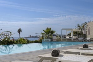 Un espace piscine avec des chaises longues, un coin salon abrité et une vue sur la mer.
