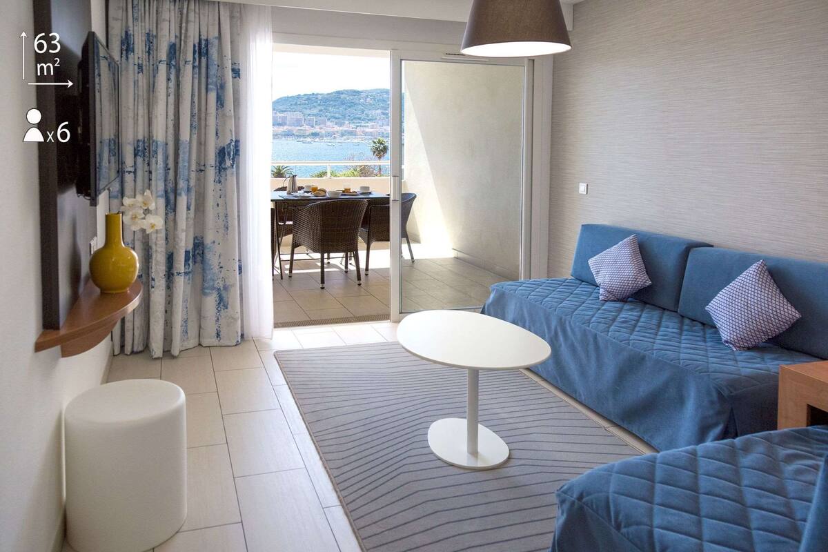 A modern room with a blue sofa, a small white table, and a view of the sea through a glass door.