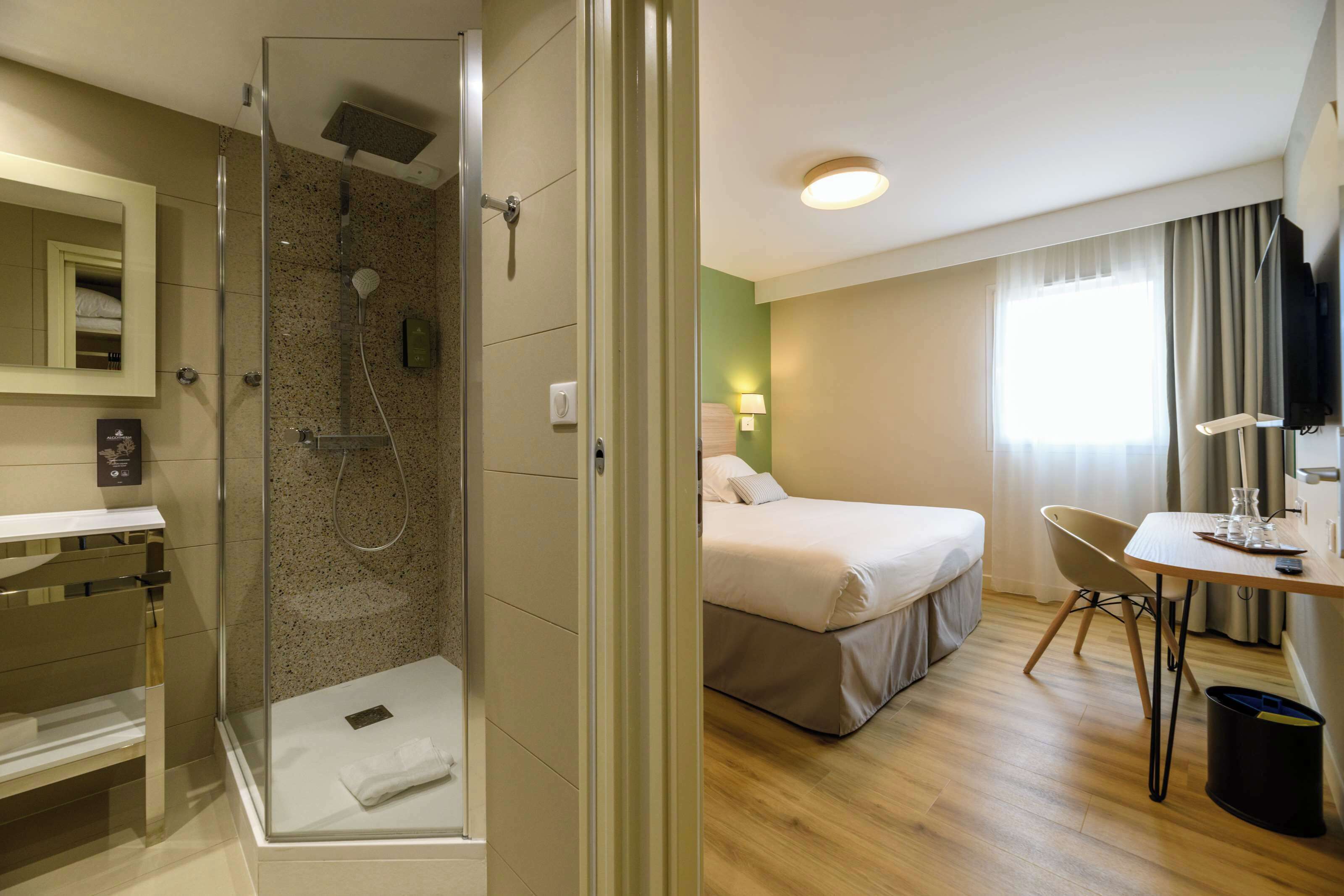 A hotel room with a shower, a bed, a desk, and a television.